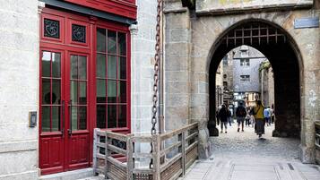 Un arco de piedra que da a una calle adoquinada, con un edificio rojo a la izquierda.