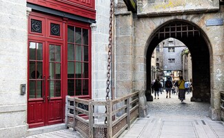 Un arco de piedra que da a una calle adoquinada, con un edificio rojo a la izquierda.