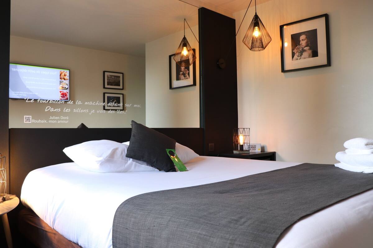Een hotelkamer met een bed, een televisie aan de muur en een ingelijst kunstwerk.
