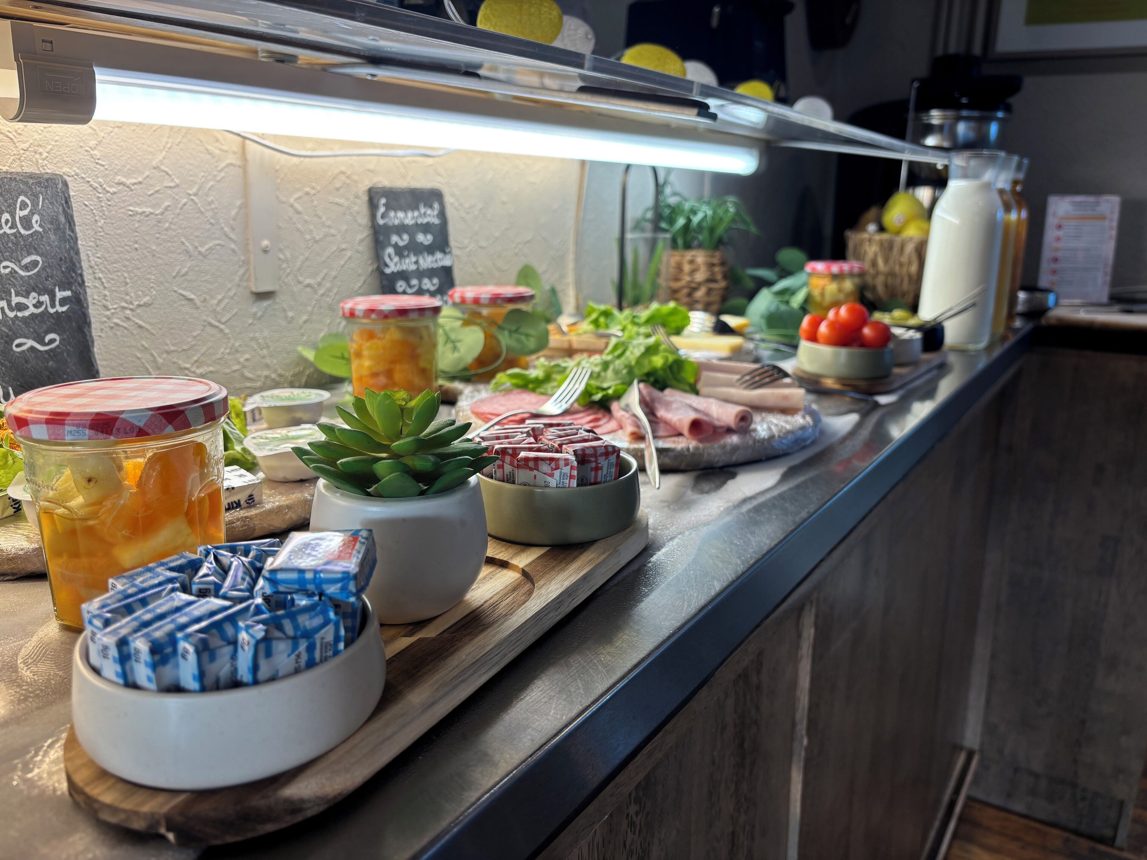 A buffet with various food items and condiments, including jars of pickles, a succulent plant, and a bowl of cheese.