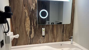 Un baño con lavamanos blanco, un espejo con luz circular y una pared de madera.