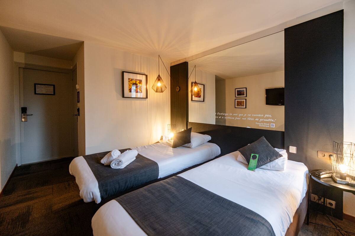 Een hotelkamer met twee bedden, een grote spiegel, lijstwerk en een nachtkastje met een lamp.