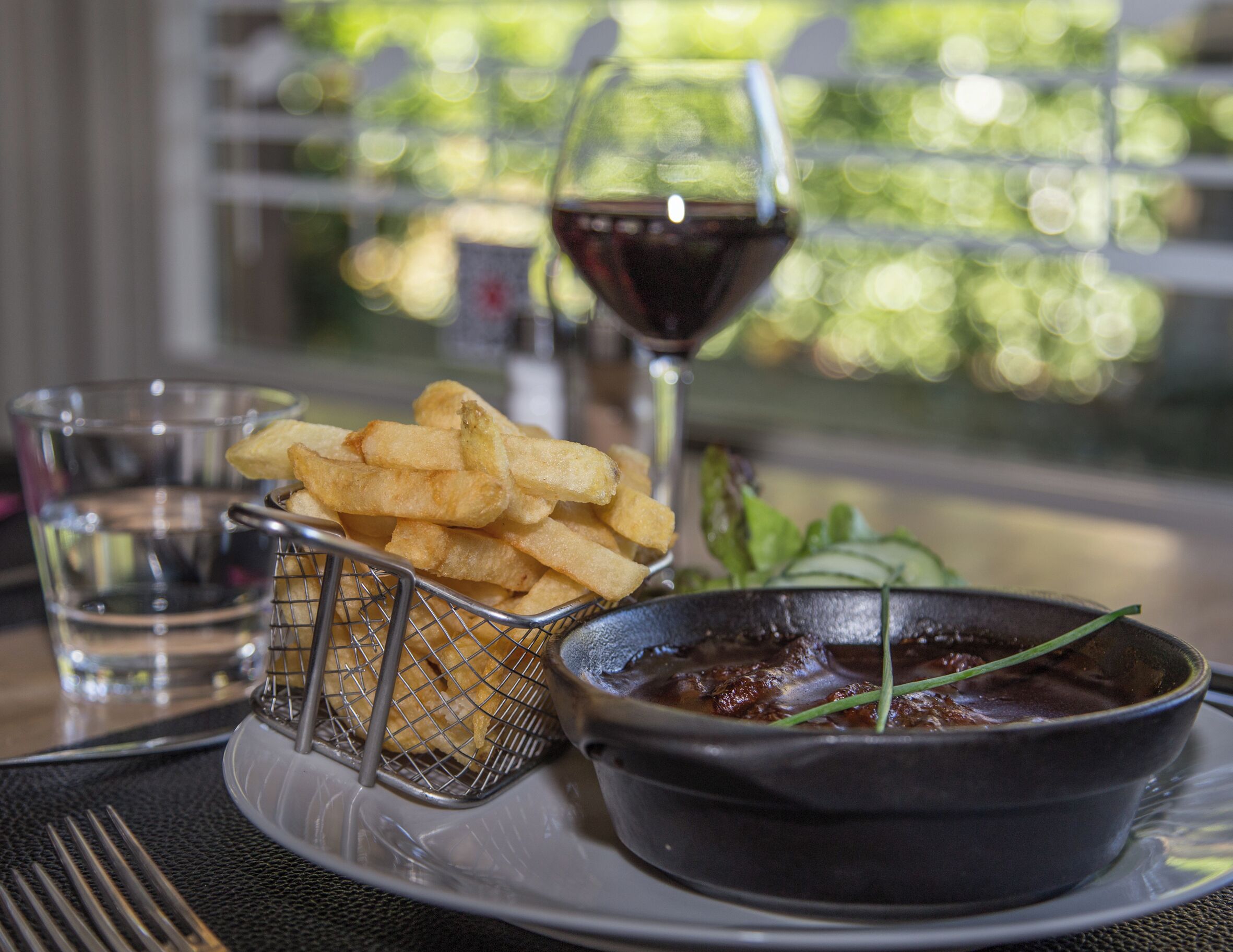 A plate with fries, a glass of red wine, and a bowl of sauce.