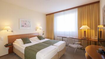 Een hotelkamer met een tweepersoonsbed, een bureau, een stoel en een groot raam met gordijnen.