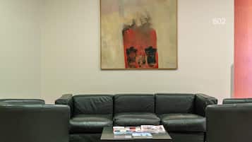 A modern living room with a black leather sofa, a coffee table with magazines, and a large abstract painting on the wall.