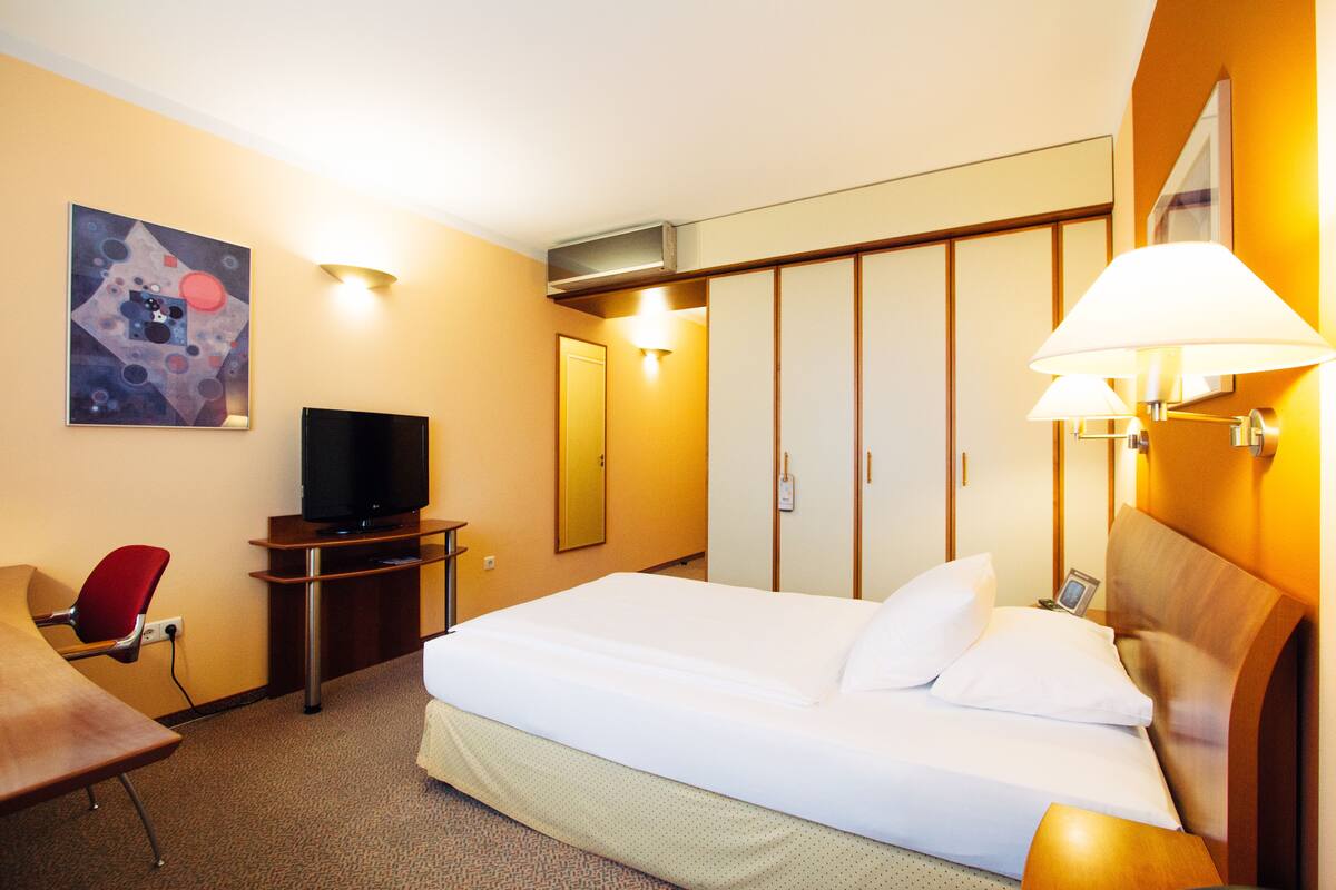 Una habitación de hotel con cama, televisión, escritorio, silla y armario.