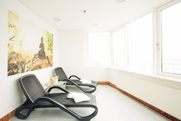 A waiting area with two black chairs, a small table with a basket, and a large window.