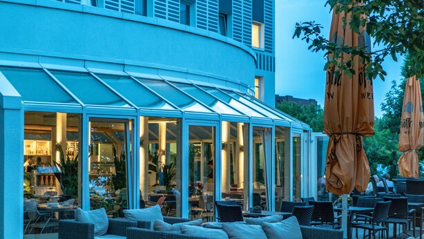 A modern outdoor seating area with wicker furniture and glass walls.