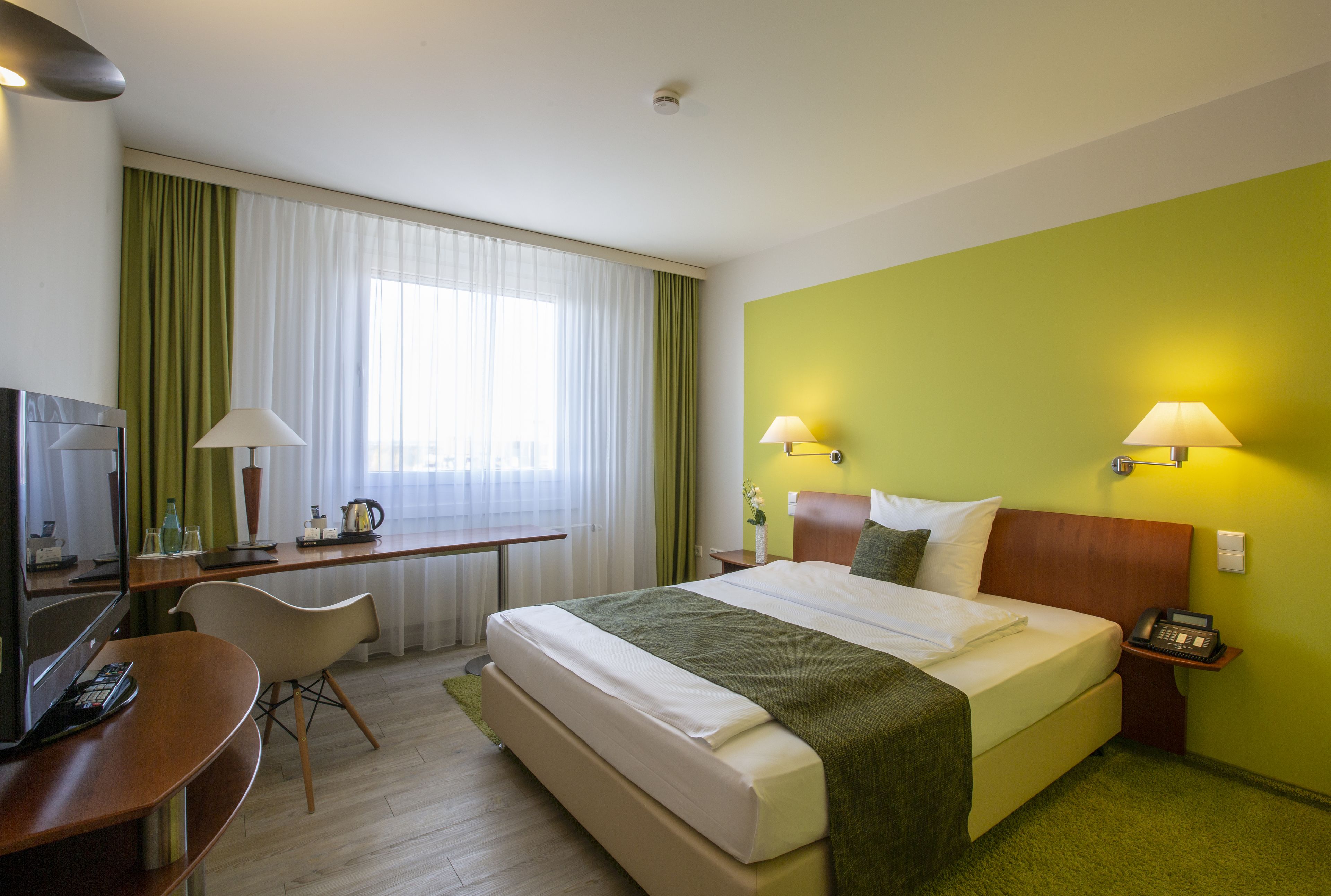 Una habitación de hotel con cama, escritorio, silla, lámparas y teléfono.