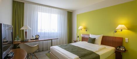 A hotel room with a bed, desk, chair, lamps, and a telephone.