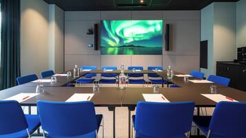 A conference room with a large screen displaying a nature scene, blue chairs, and a long table with water bottles and nameplates.