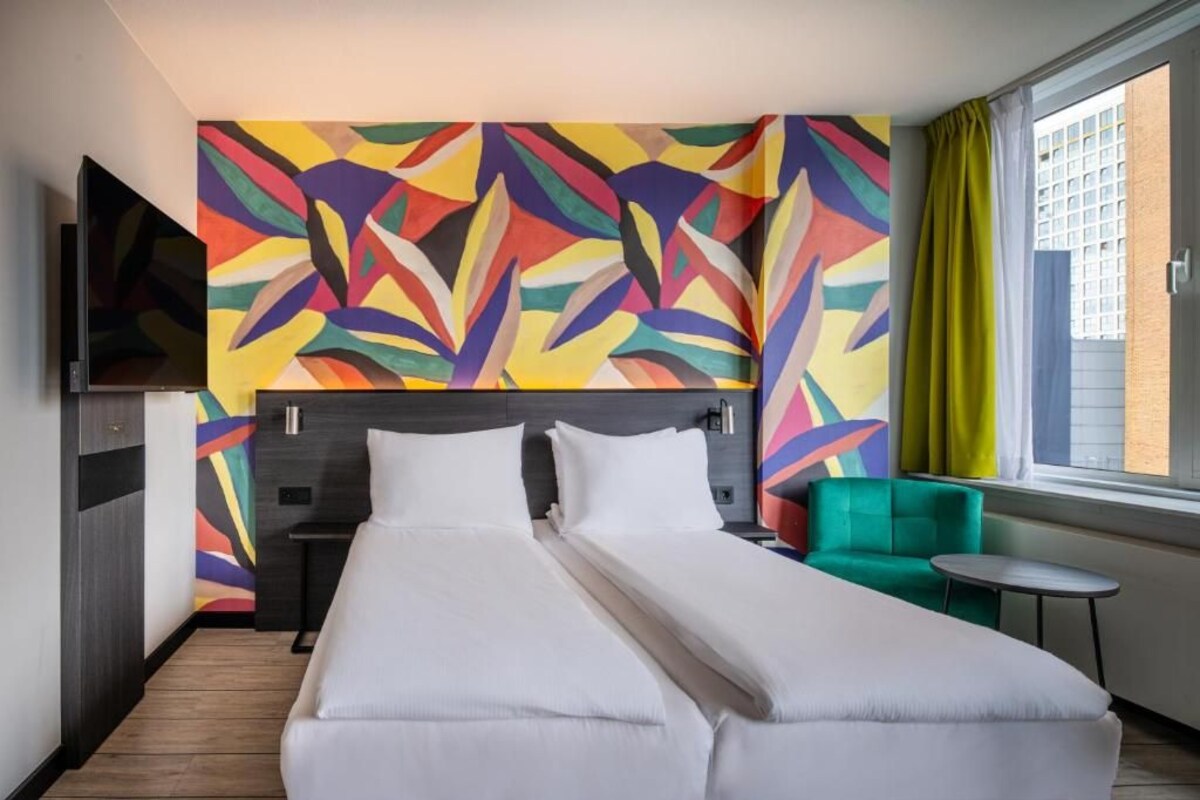 A hotel room with a large bed, a green armchair, and a small table.