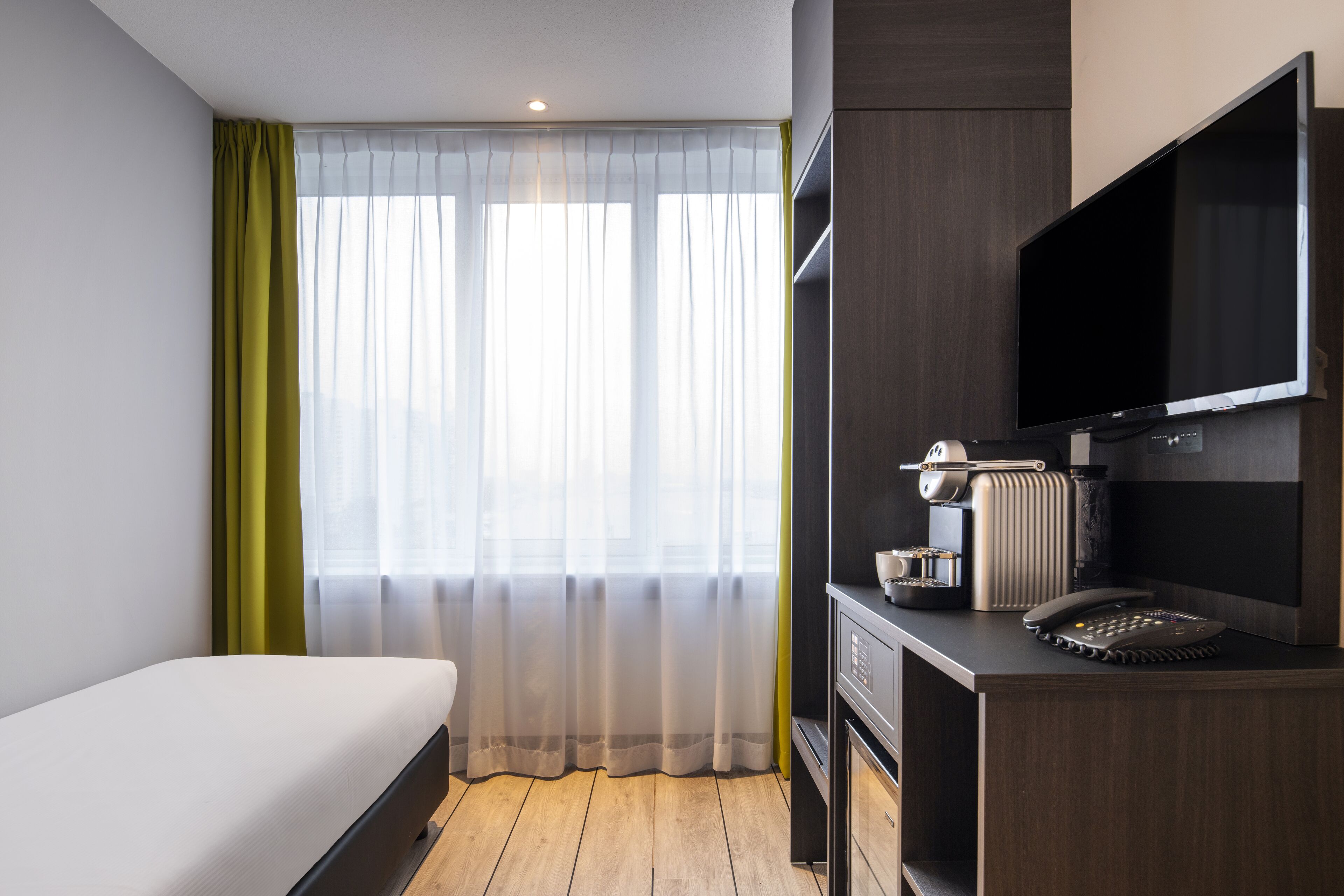 Een hotelkamer met een bed, een bureau met telefoon, een koffiezetapparaat en een televisie.