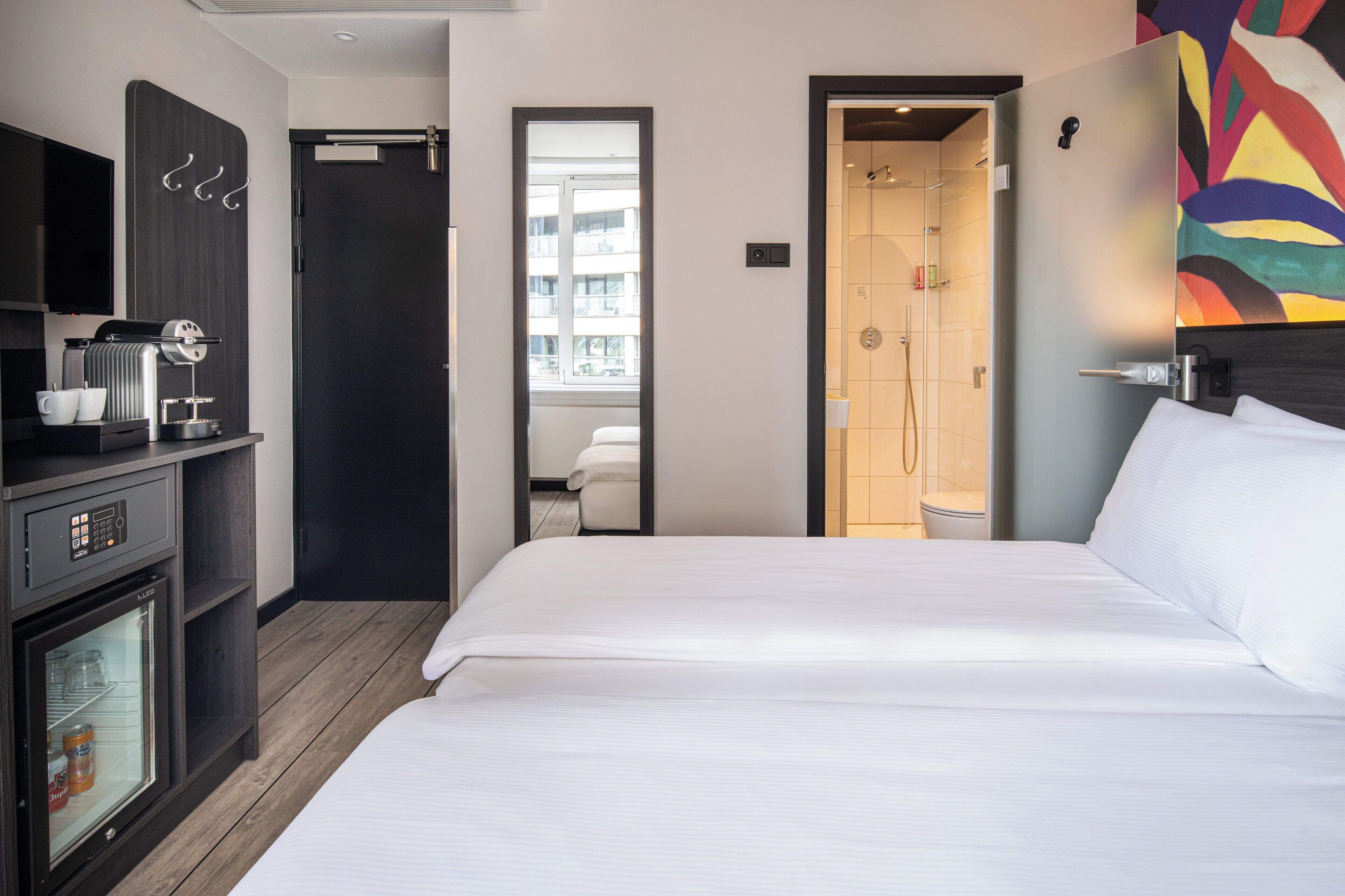 Een hotelkamer met een bed, een koffieapparaat, een televisie en een douche.