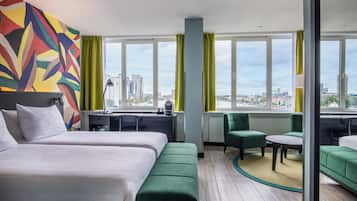A hotel room with two beds, a desk, a chair, a sofa, and a view of the city.