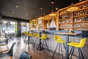 Una zona de bar con estantes de madera llenos de botellas, un modelo de velero y taburetes amarillos.