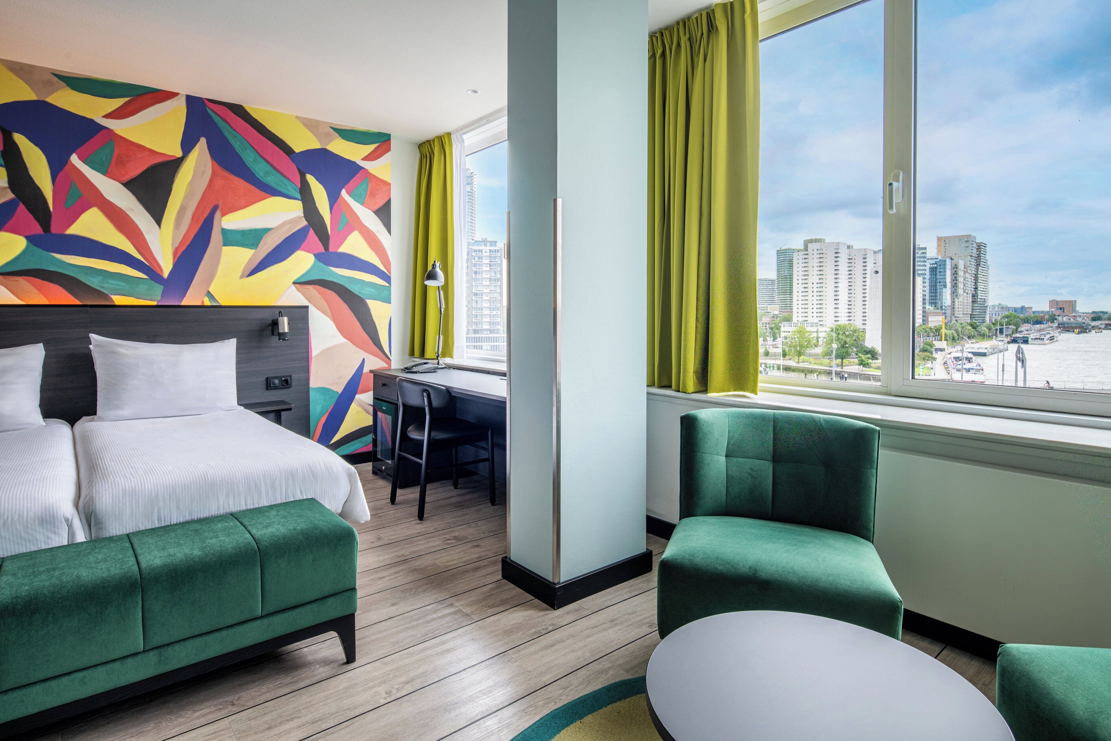A hotel room with a bed, a desk, a chair, and a view of the cityscape.