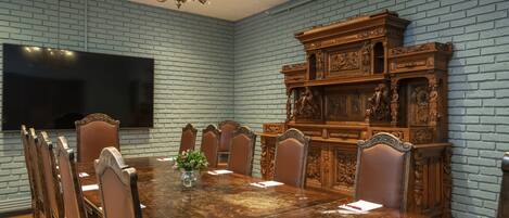 A conference room with a large wooden table, six chairs, a television, and a decorative wooden cabinet.