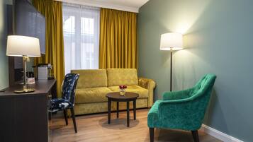Habitación de hotel con sofá, una silla, una mesita con un jarrón, un escritorio con lámpara y una lámpara de pie.
