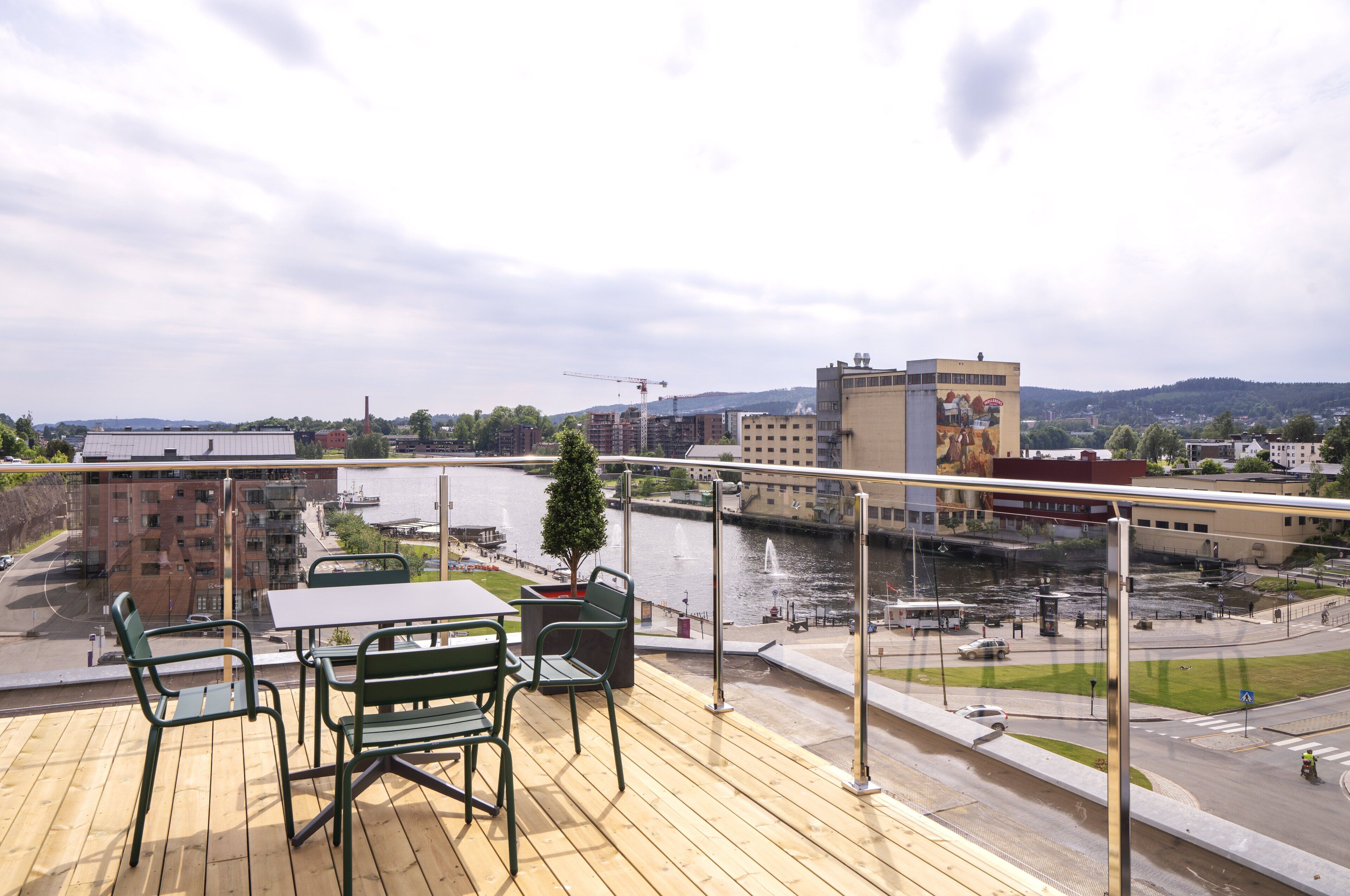 A balcony with a table and chairs overlooking a river, with buildings and a bridge in the background.