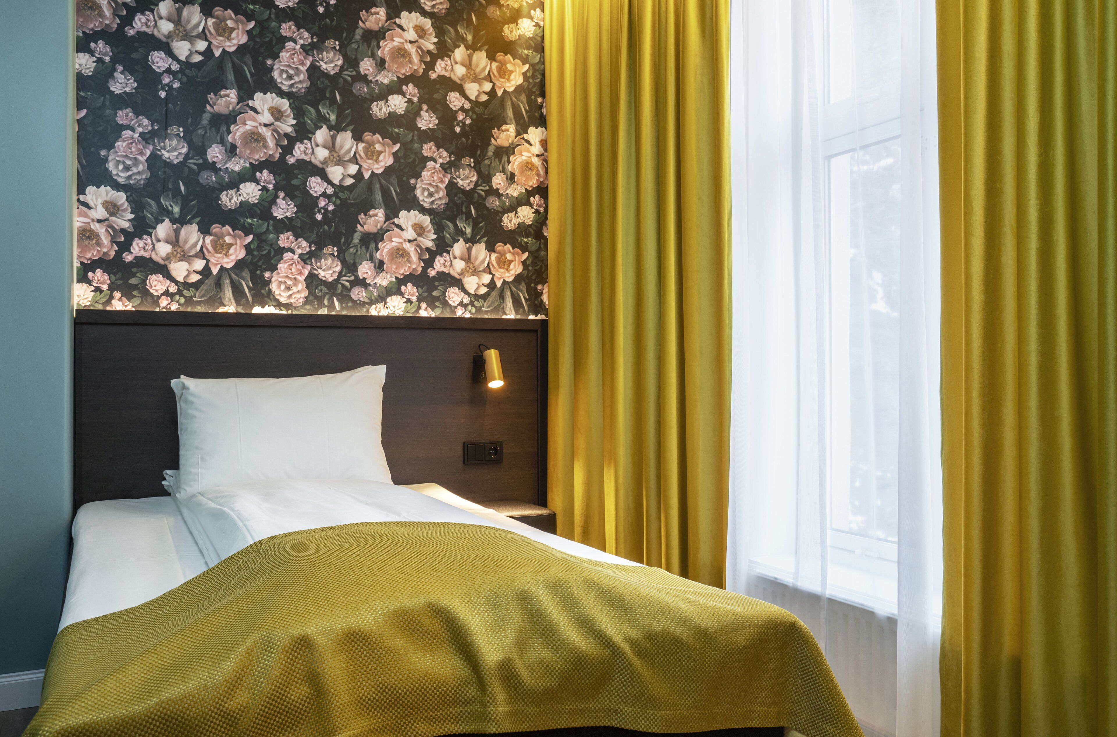 A neatly made bed with white linens, a dark headboard, and a floral wallpaper pattern.