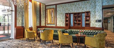 A lobby with a green sofa, yellow chairs, a chandelier, and a patterned carpet.