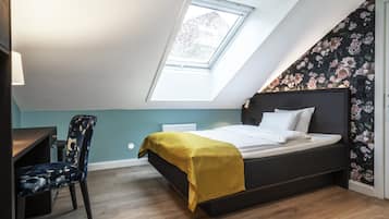 A bedroom with a skylight, a bed with a yellow blanket, a desk with a chair, and floral wallpaper.