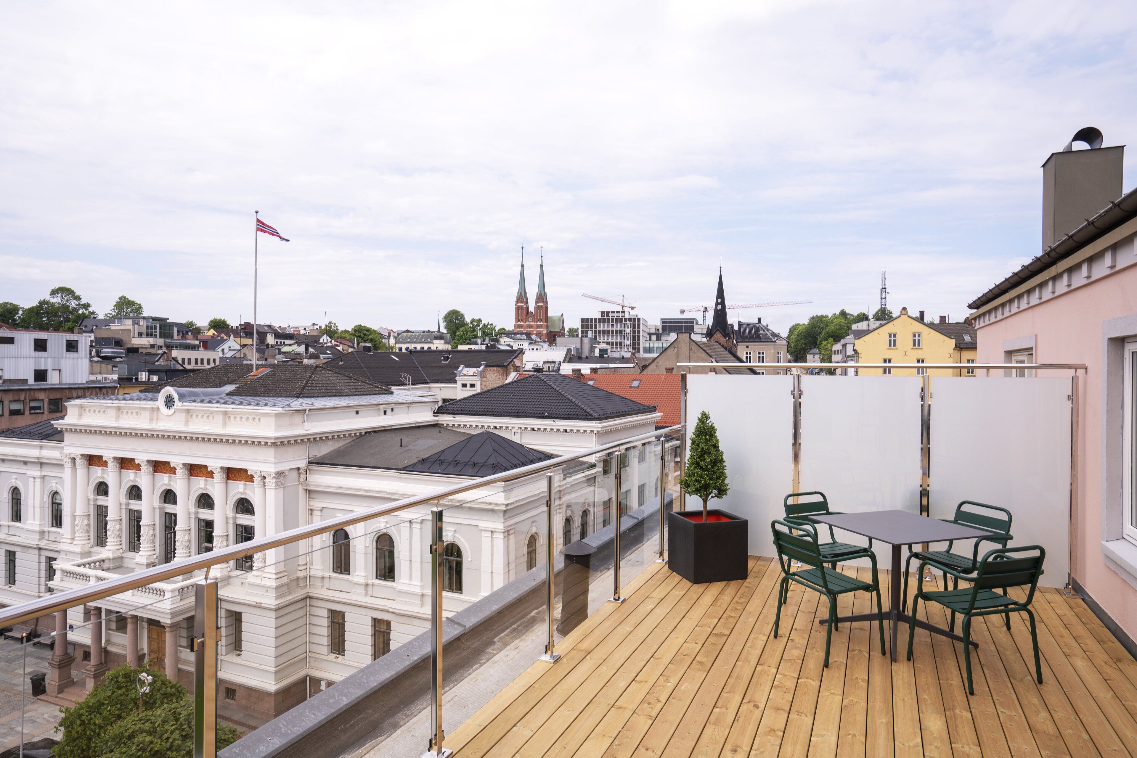 A rooftop terrace with a wooden deck, a table with chairs, and a potted plant.