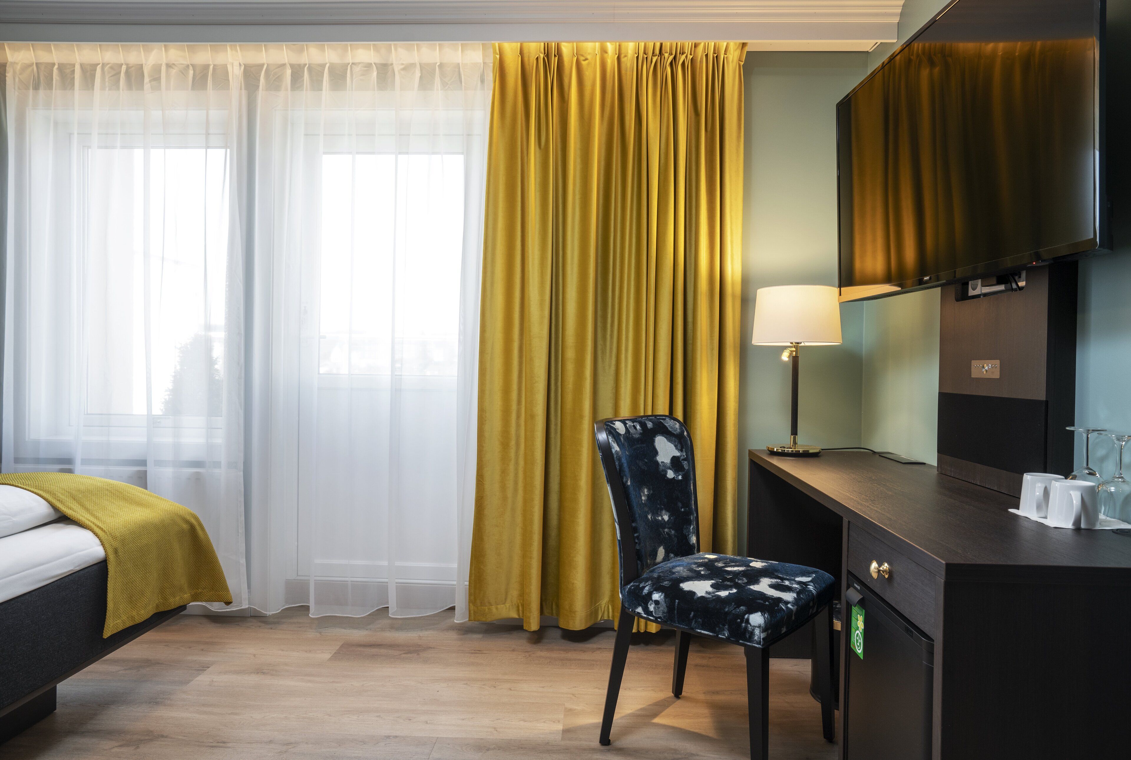 A hotel room with a bed, a desk with a lamp, a chair, and a television.