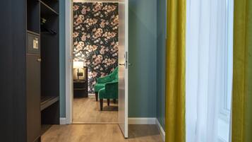 A room with a floral wallpaper, a green armchair, and a wooden floor.