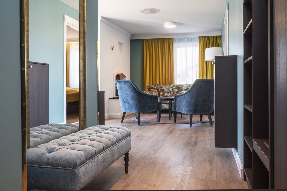 Et hotelværelse med en knapbetrukken skammel, et spisebord med to stole og et stort spejl.