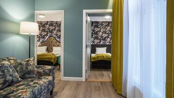 Ett rum med en soffa med blommönster, en säng med ett grönt överkast och en sänggavel med en tapet med blommönster.
