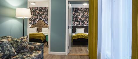 A room with a floral-patterned sofa, a bed with a green bedspread, and a headboard with a floral wallpaper design.