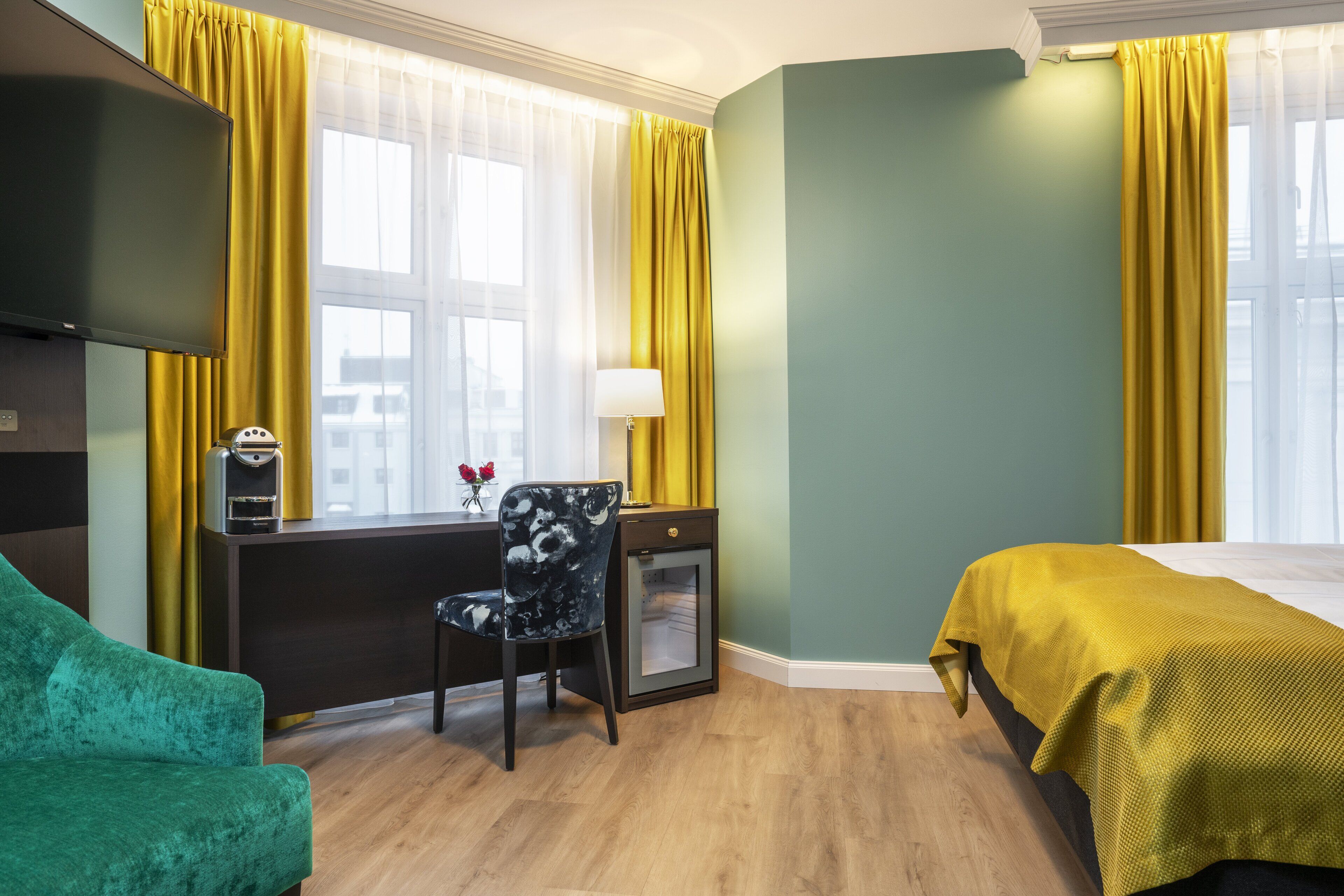 Ein Hotelzimmer mit Bett, Schreibtisch mit Stuhl, Fernseher und einem Fenster mit Vorhängen.