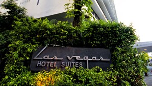 Een hotelsbord met de naam 'Las Vegas Hotel Suites', omringd door weelderige begroeiing en palmbomen.