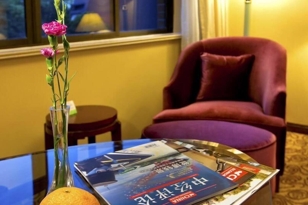 Una habitación de hotel con una mesa de vidrio que muestra una revista, un florero con flores y una naranja.