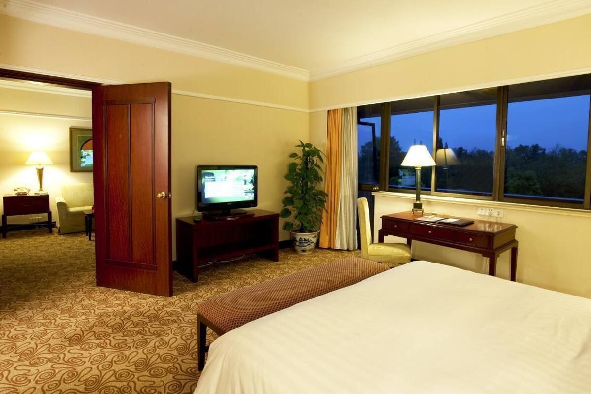 Habitación de hotel con una cama grande, un escritorio con lámpara, televisión y vistas al exterior a través de una ventana.