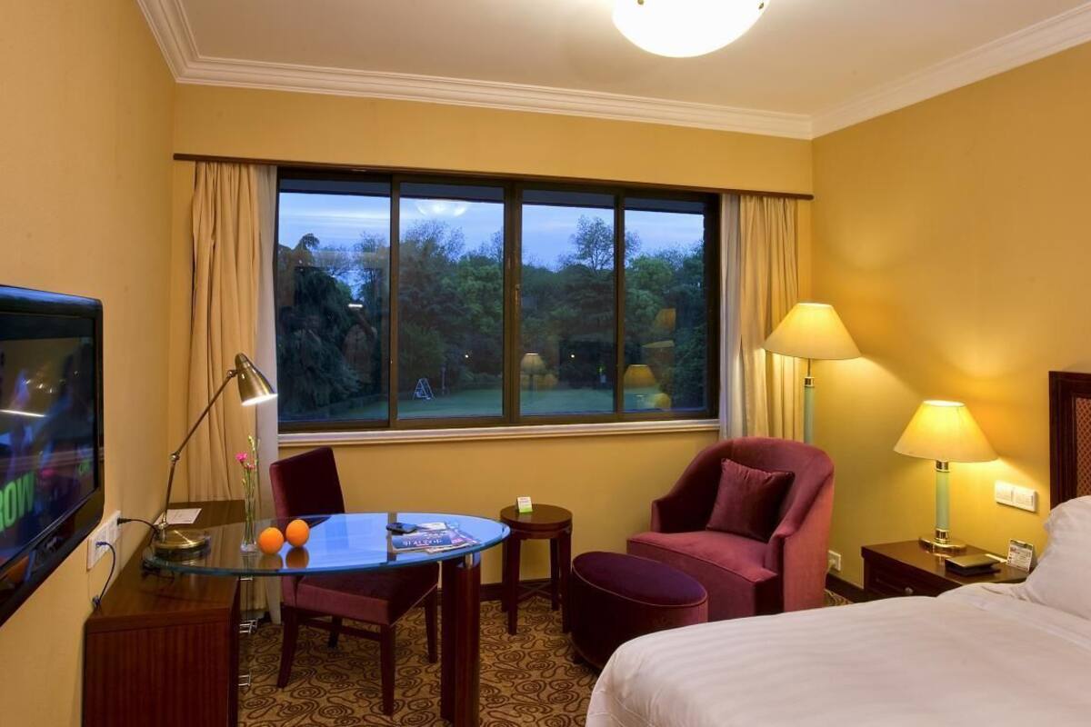 Habitación de hotel con una cama, un escritorio con computadora, una silla, una mesita y un televisor.