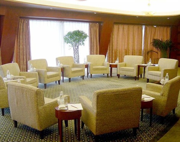 Habitación de hotel con una zona de estar circular, varios sillones, una mesita y un ventanal grande con cortinas.