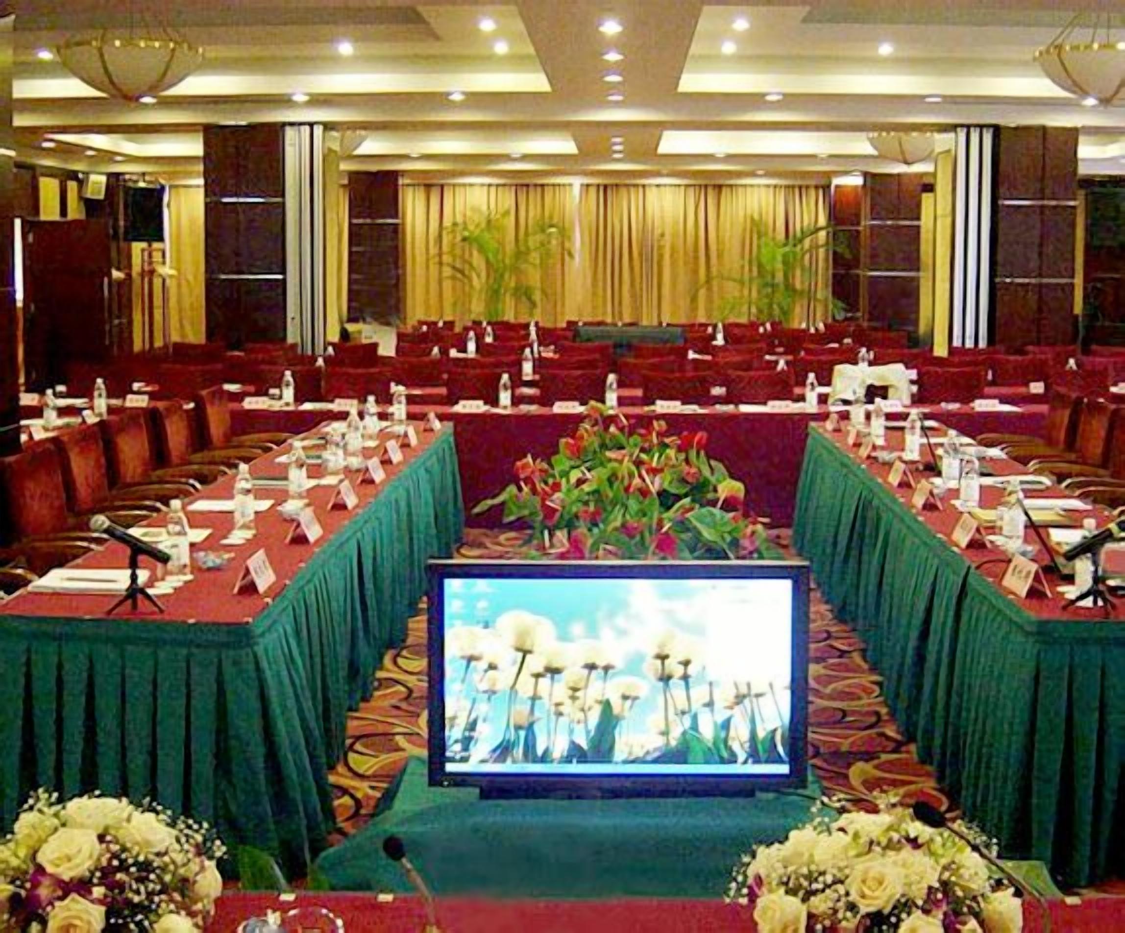 A conference room with rows of tables, microphones, and a large screen at the front.