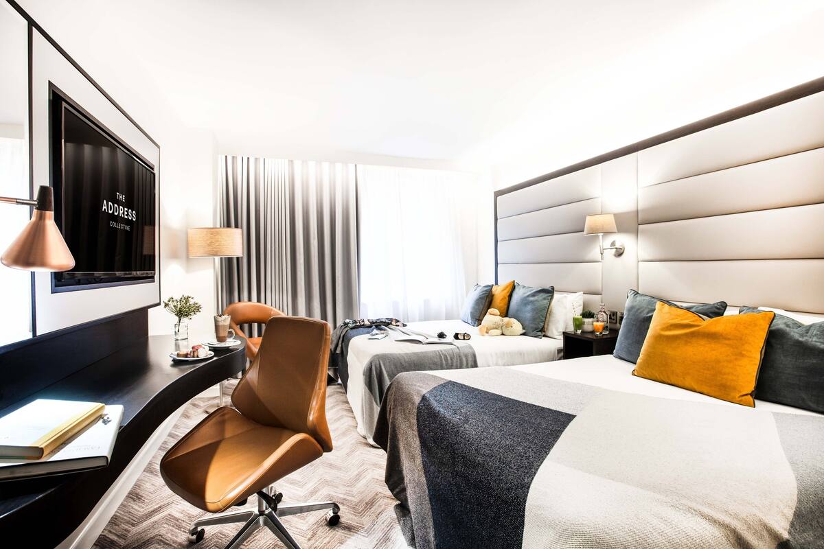 Una camera d'albergo con un letto, due comodini, una scrivania con una sedia, una televisione e una finestra con tende.