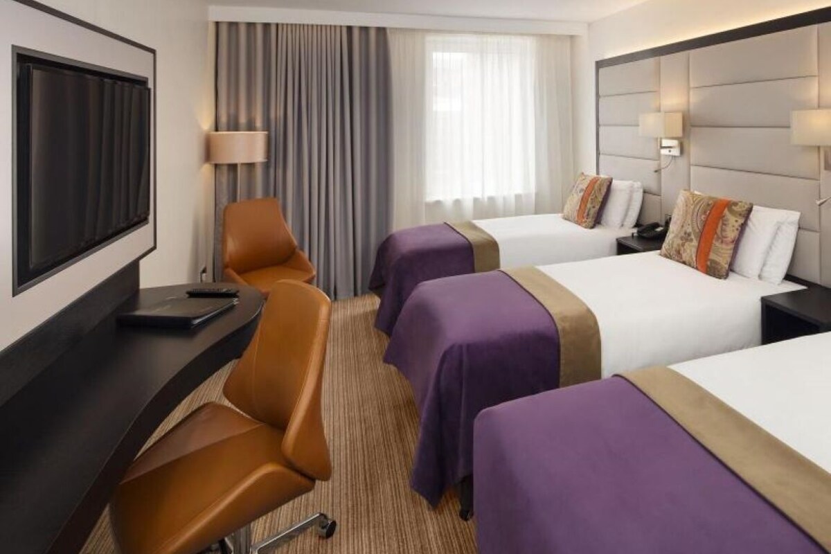 Une chambre d’hôtel avec deux lits, un bureau avec une chaise, une télévision et une fenêtre avec des rideaux.