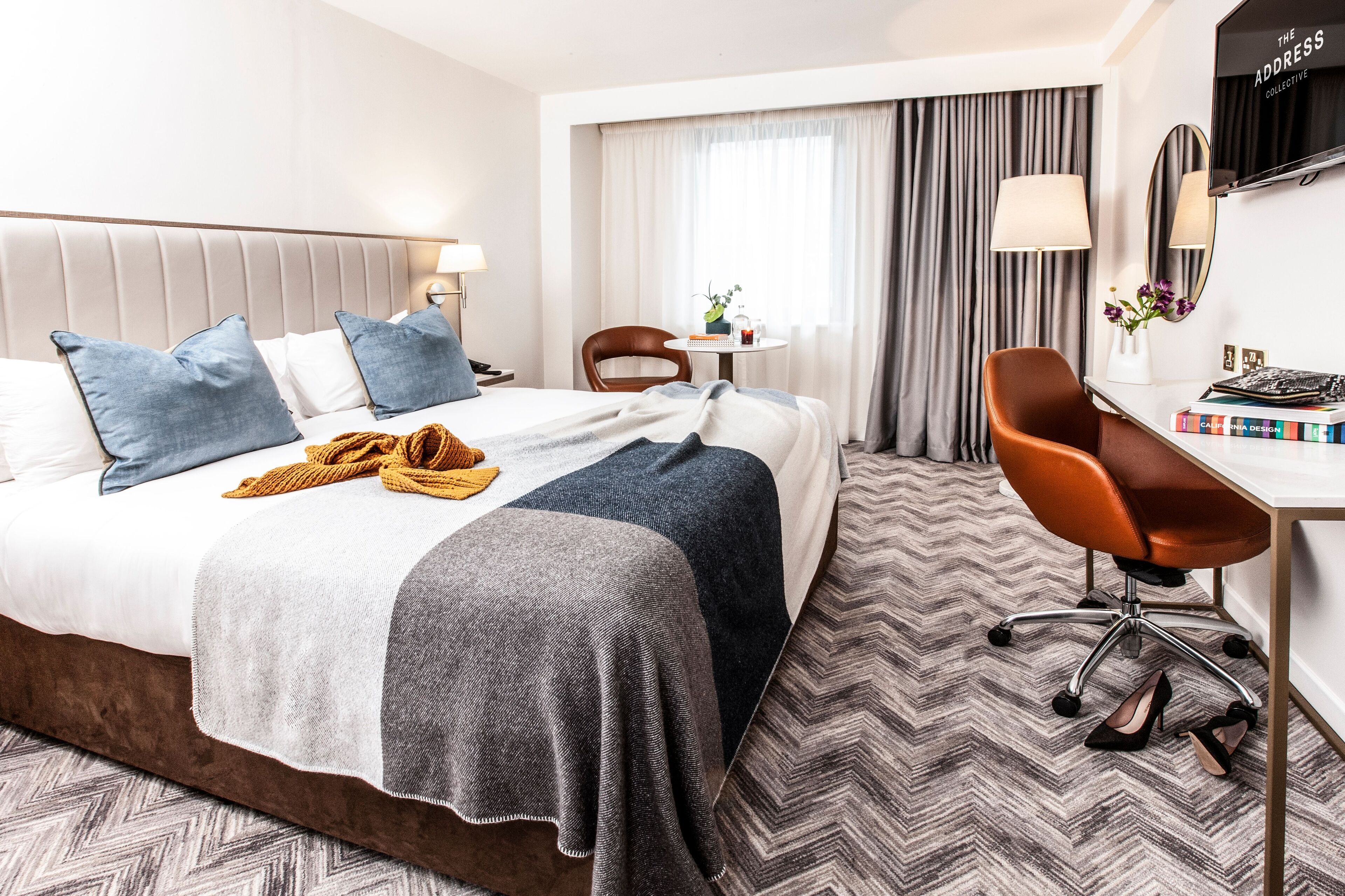 A hotel room with a bed, a desk, a chair, and a window with curtains.