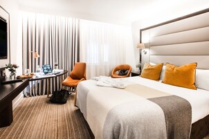 Una habitación de hotel con una cama, un escritorio, una silla anaranjada, un televisor y una ventana con cortinas.