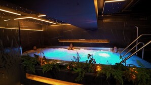 Un jacuzzi con tres personas, rodeado de plantas e iluminación moderna.