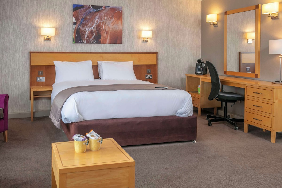 A hotel room with a bed, a desk, a chair, a small table, and a mirror.