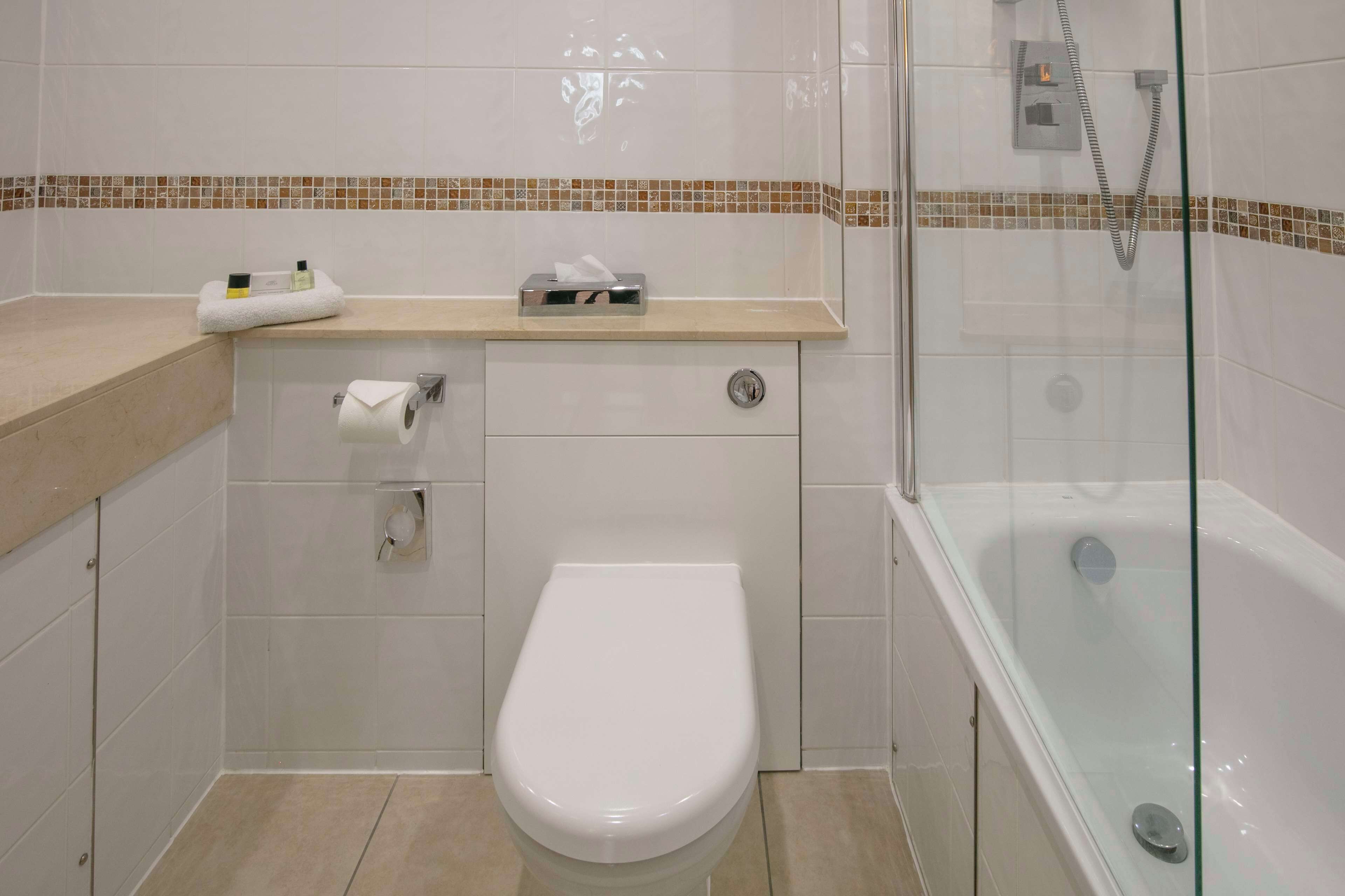 A bathroom with a toilet, a glass-enclosed shower, and a vanity with a towel and toiletries.