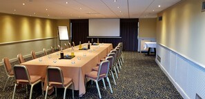 Une salle de conférence équipée d’une longue table, de chaises, d’un écran de projection et d’un tableau blanc.