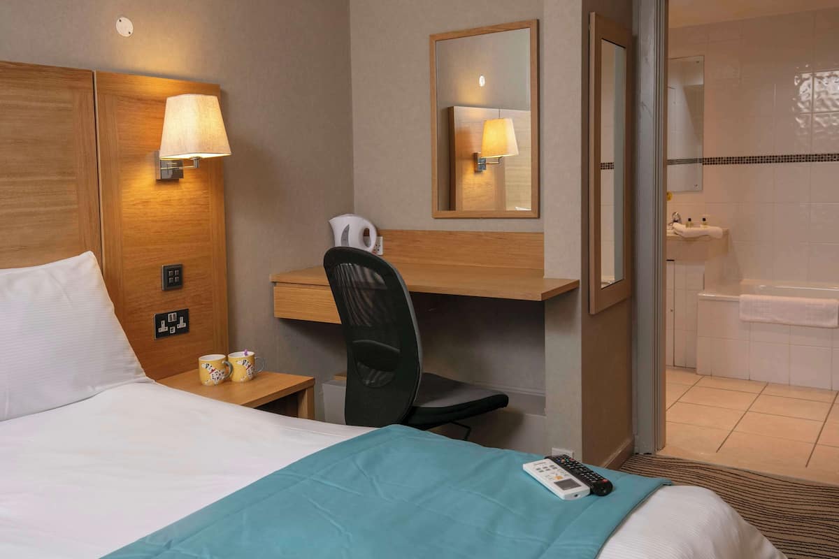 A hotel room with a bed, desk, chair, and a bathroom visible through an open door.