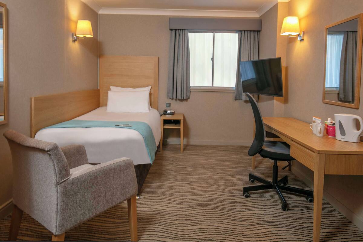 A hotel room with a bed, a desk with a chair, a television, and a coffee maker.